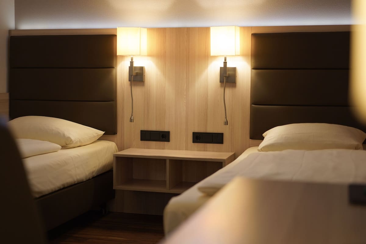 A hotel room with two beds, a wooden headboard, and two wall-mounted lamps.