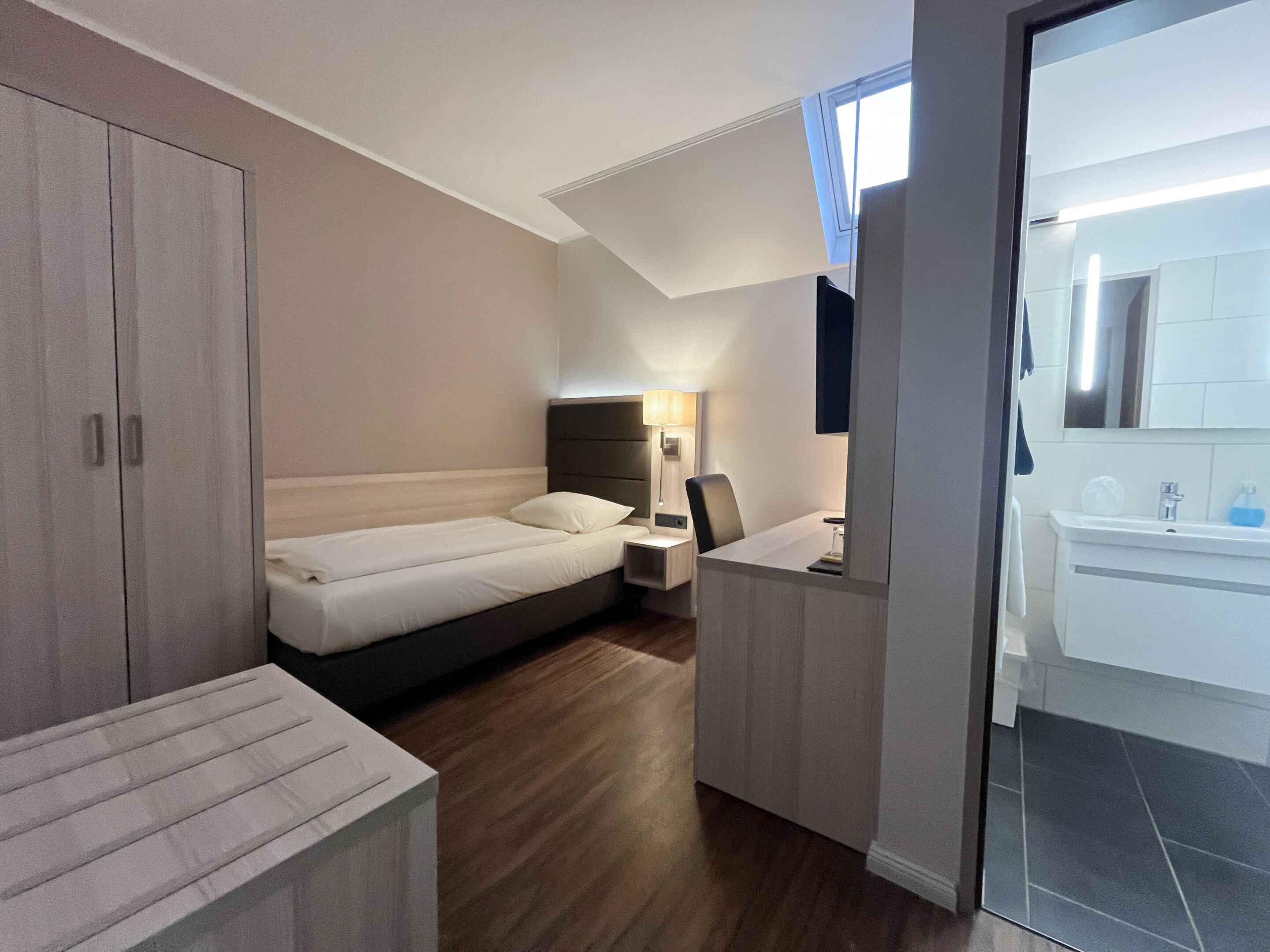 Un hotel moderno con cama, mesita de noche, lámpara y vistas al baño.