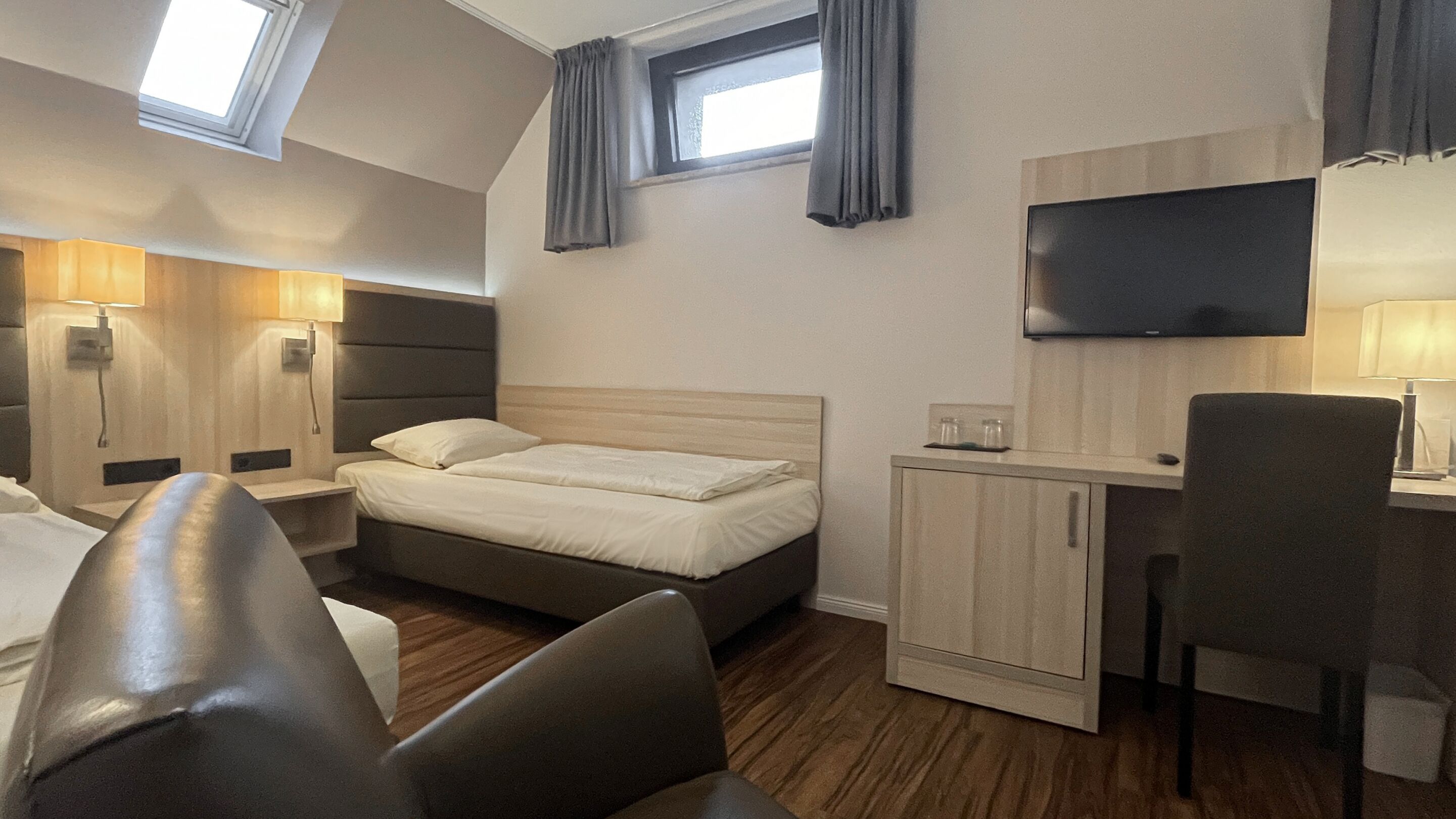 Ein Hotelzimmer mit Bett, Schreibtisch, Stuhl, Fernseher und einem Fenster mit Vorhängen.