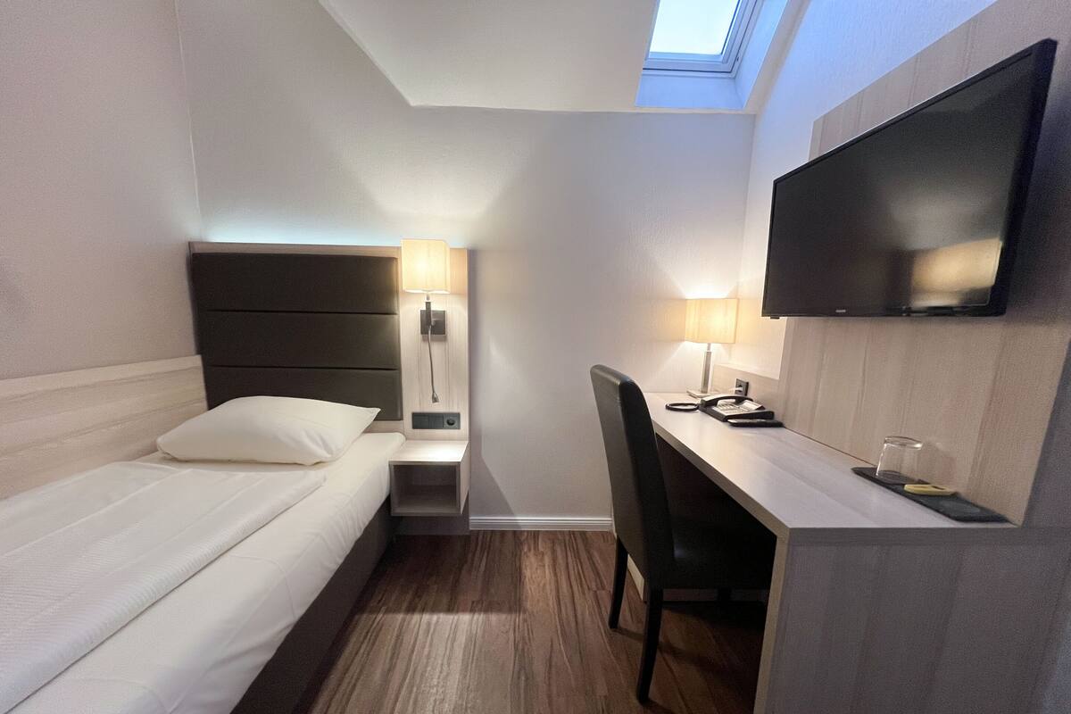 A hotel room with a bed, desk, chair, lamp, TV, and a skylight.