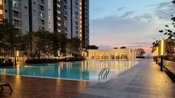 Una piscina con borde de baldosas, rodeada de árboles y edificios modernos.