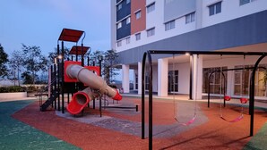 Un parque infantil con toboganes y columpios, rodeado por un edificio con ventanales amplios.