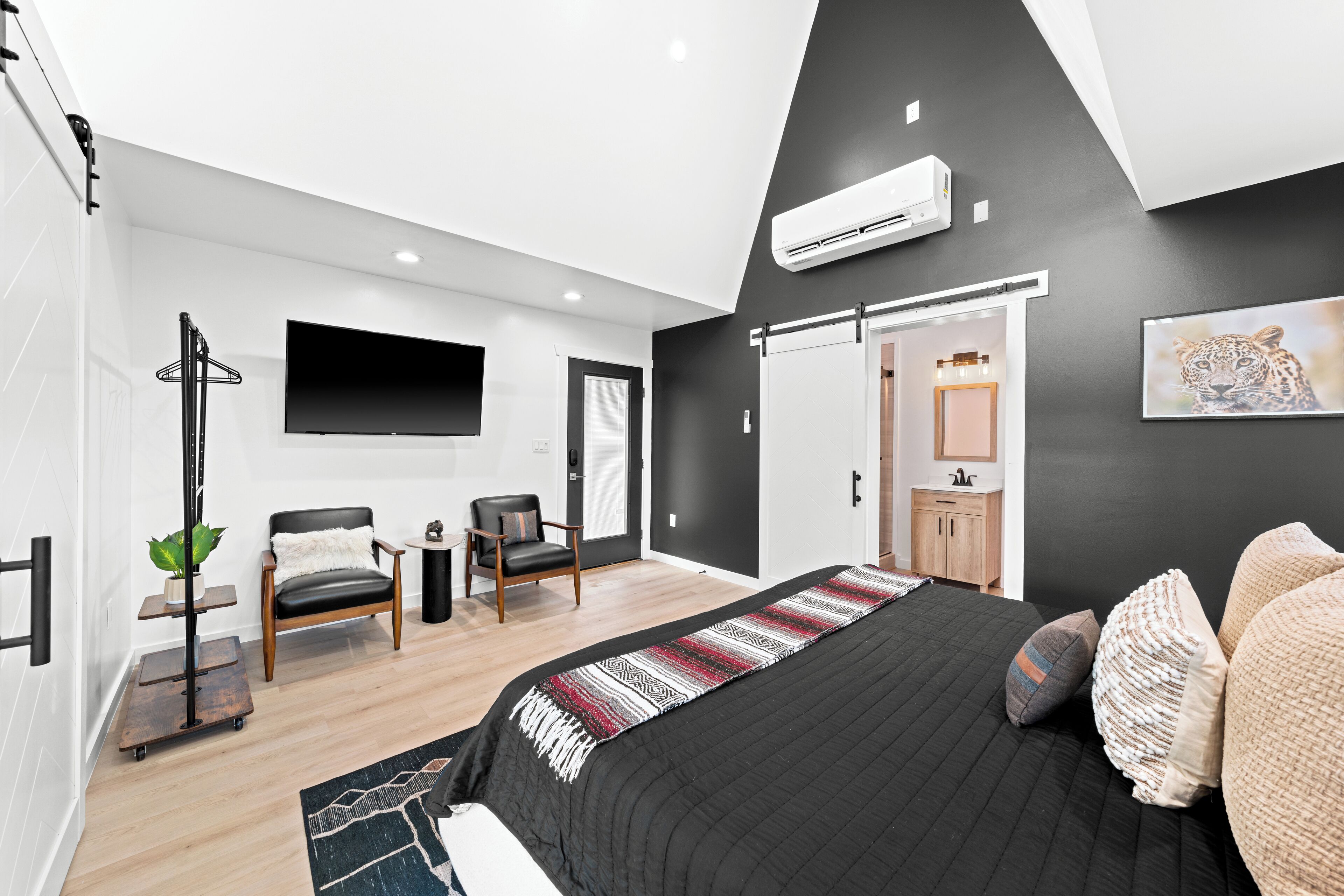 A modern bedroom with a large bed, a TV, a chair, a desk, and a wardrobe.
