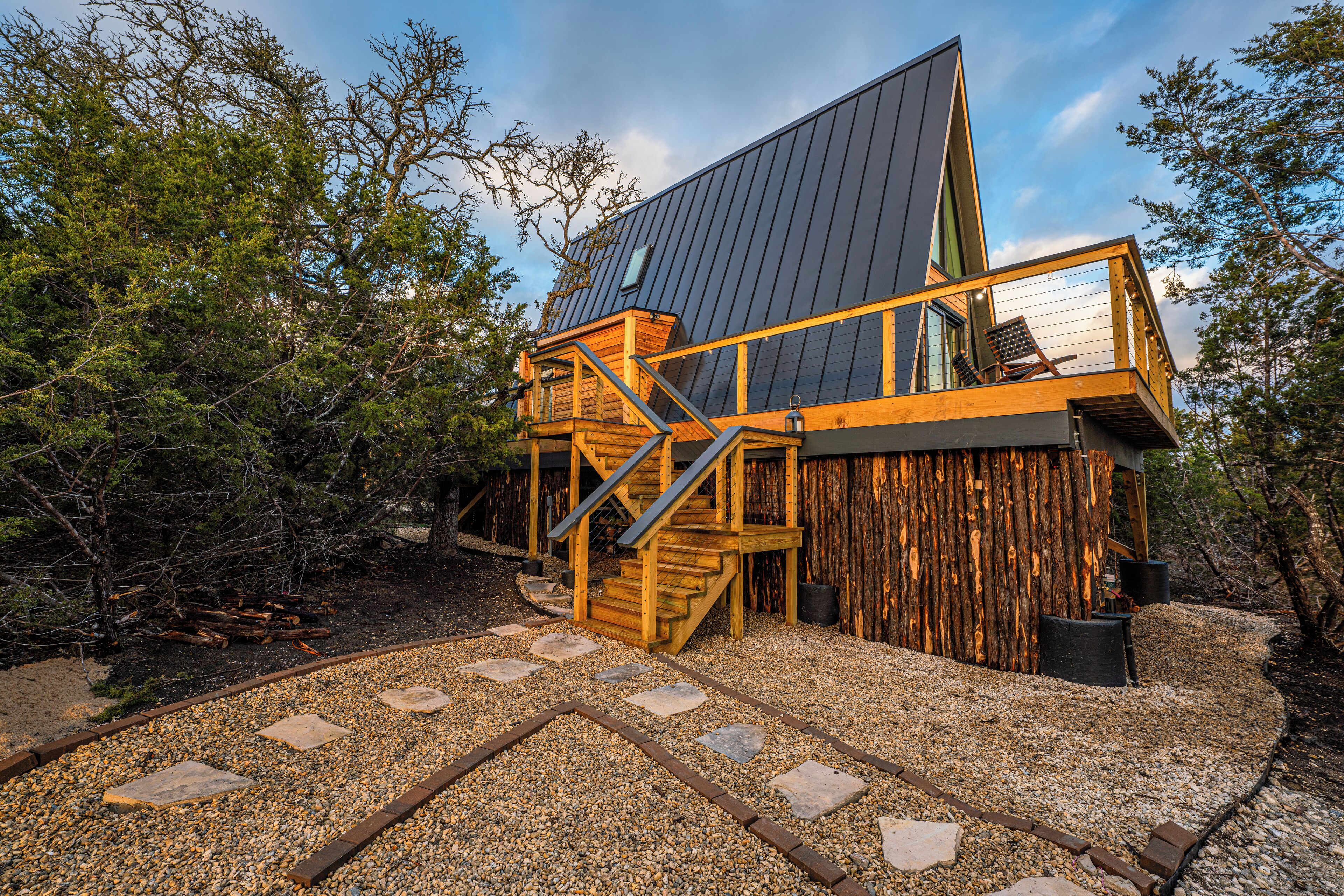 A modern wooden cabin with a sloped roof, a wooden staircase, and a gravel pathway leading to the entrance.