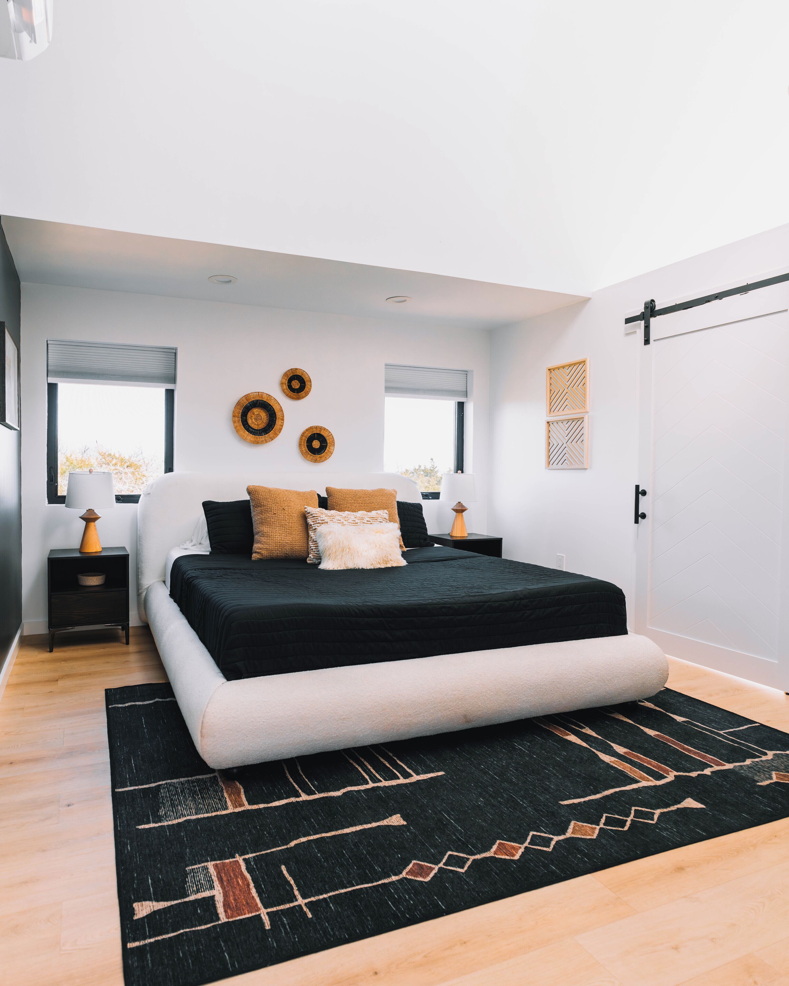 Un dormitorio moderno con una cama grande, una paleta de colores blanco y negro y una alfombra negra con diseños geométricos.