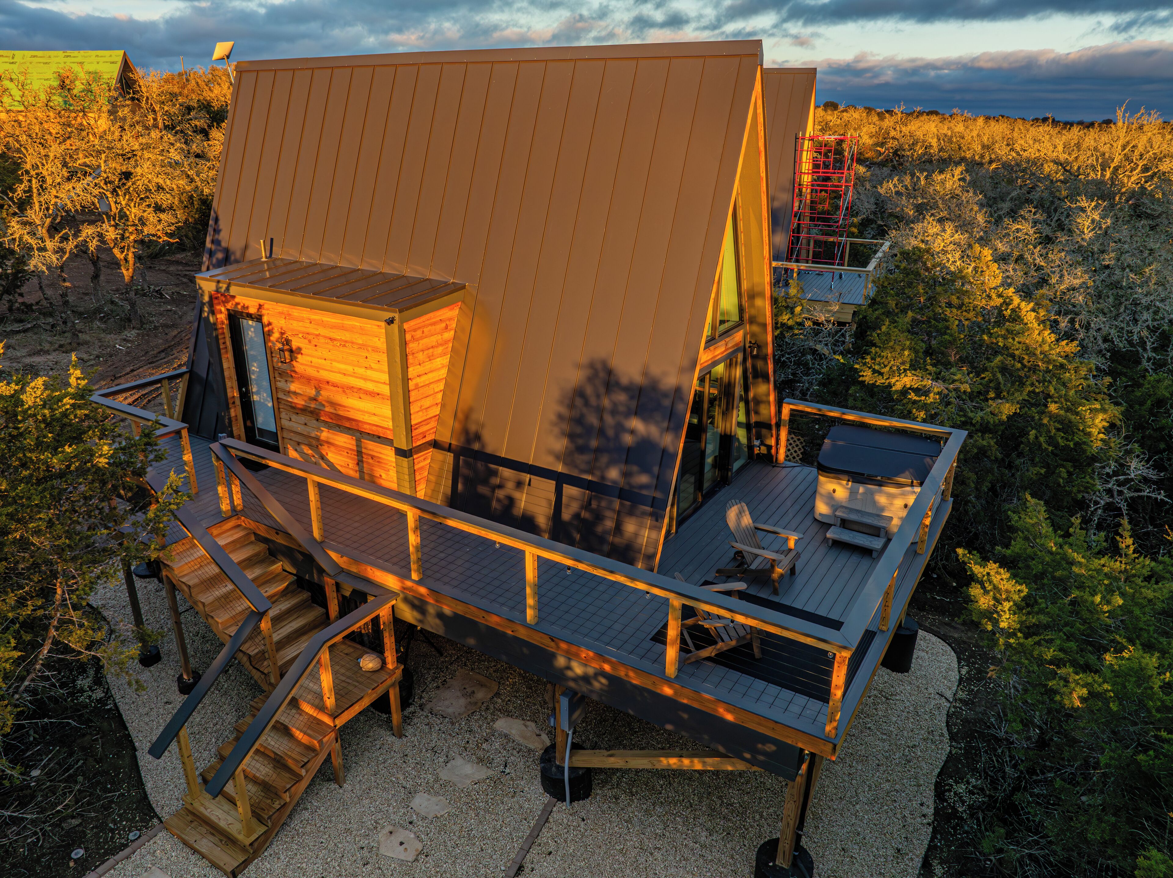 Une cabane moderne en bois dotée d’une grande terrasse, d’un bain à remous et d’un escalier menant à l’entrée principale.