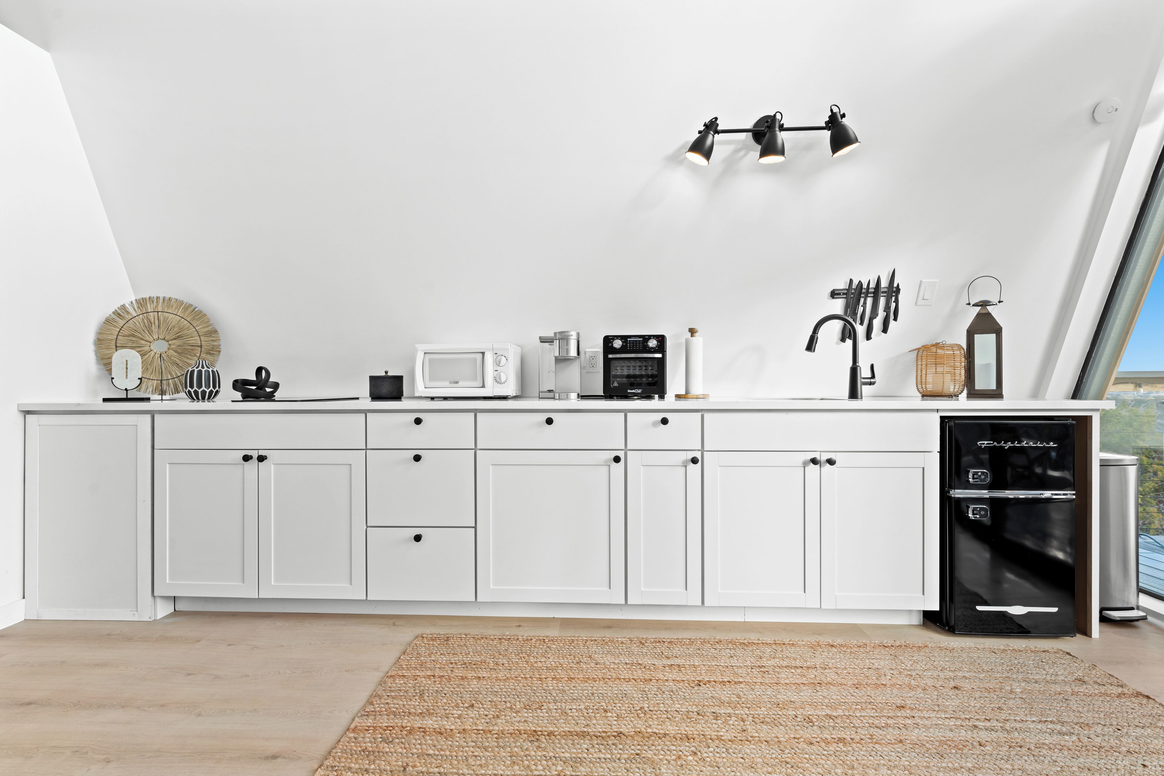 A modern kitchen with white cabinets, a black refrigerator, and a large window.