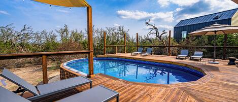 A wooden deck with a swimming pool, lounge chairs, and a covered area with a table and chairs.