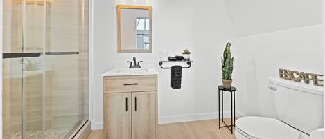 A modern bathroom with a glass shower enclosure, a wooden vanity, a toilet, and a small potted plant.