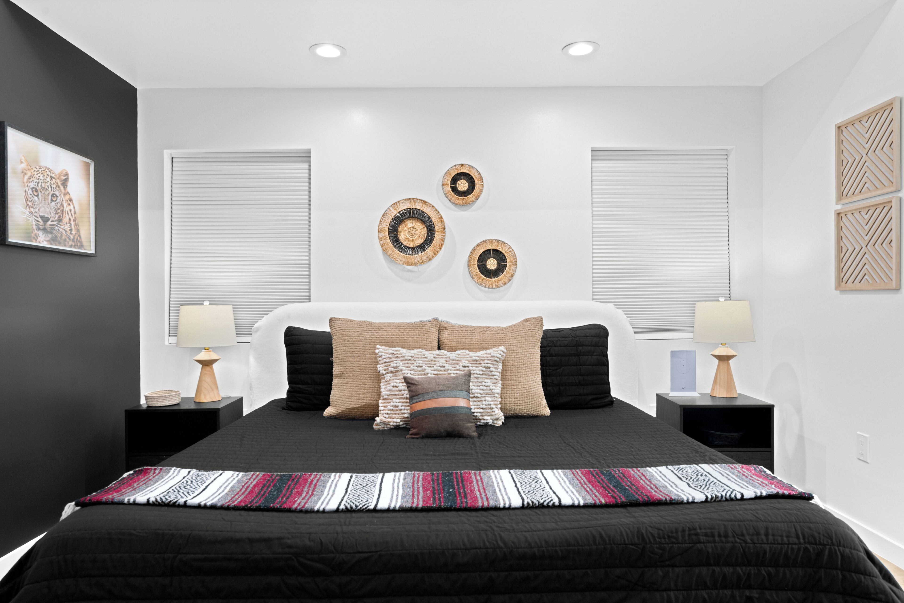 Une chambre à coucher moderne avec un lit noir, deux tables de chevet avec des lampes, une grande horloge murale et un tableau encadré.