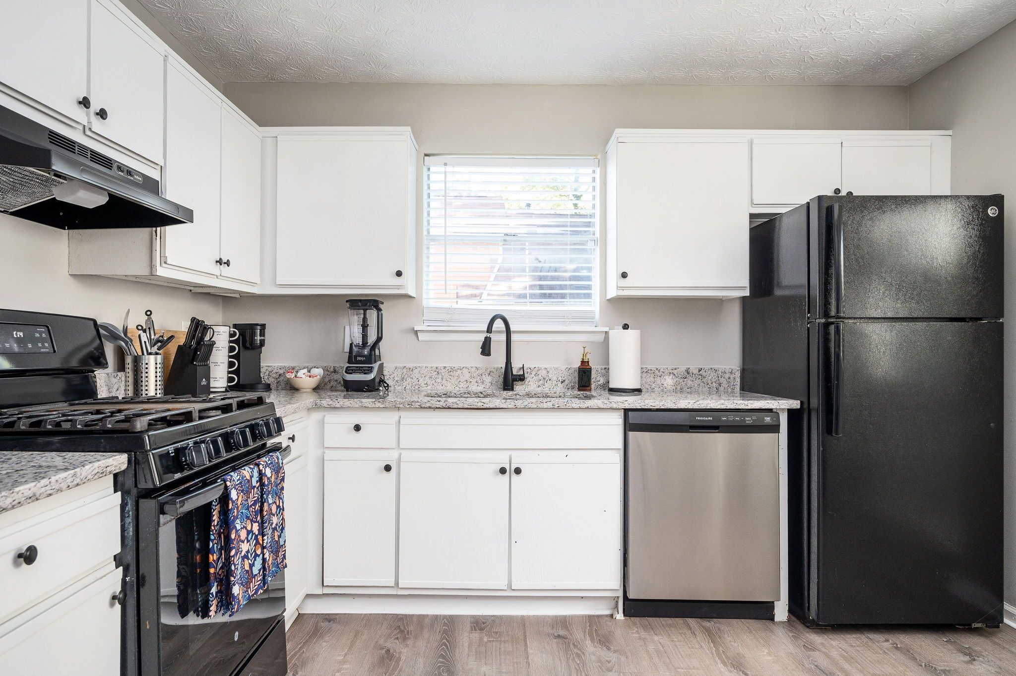 A modern kitchen with white cabinets, a black refrigerator, stainless steel dishwasher, and a gas stove.