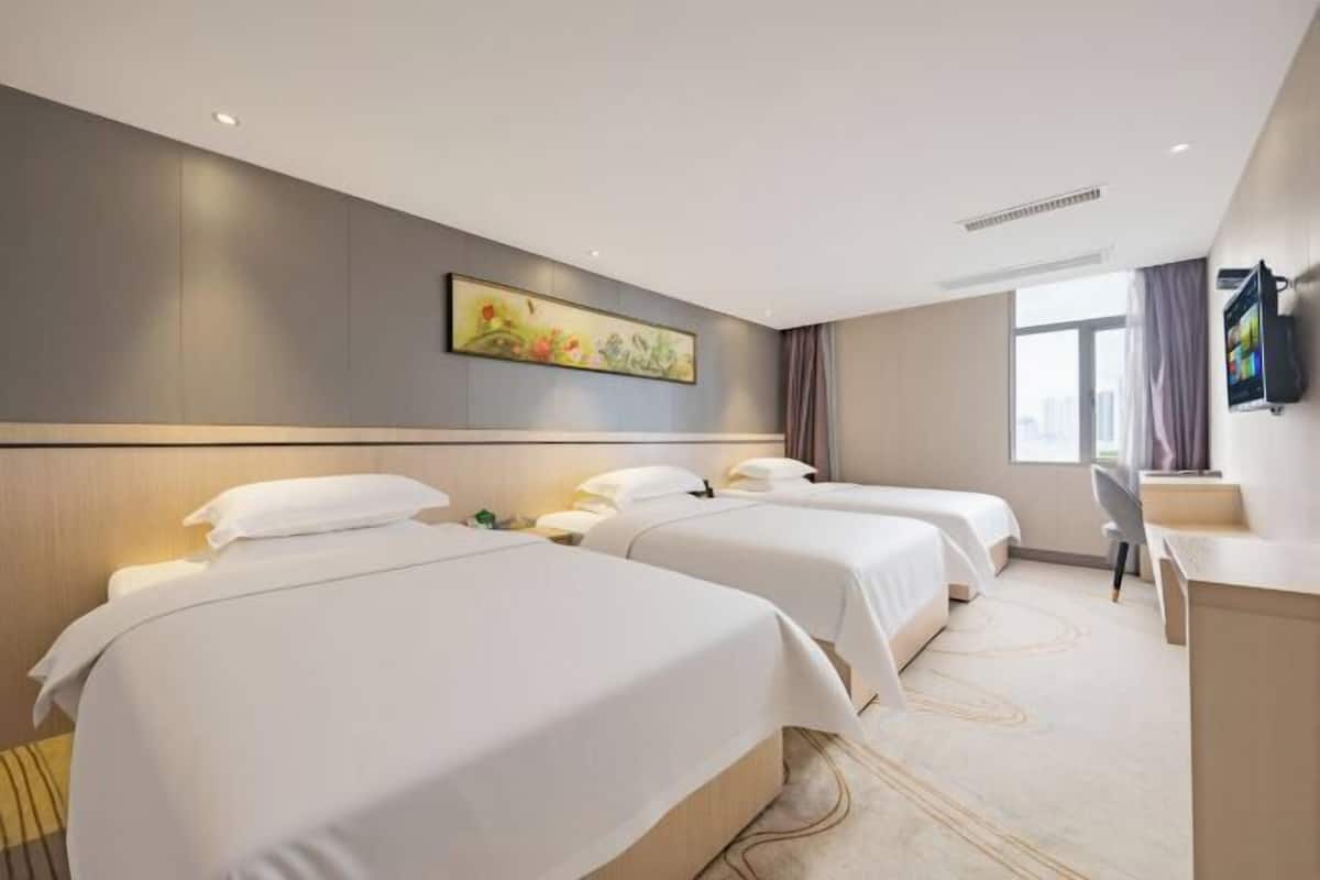Una camera d'albergo con due letti, una scrivania, una sedia, una televisione e una finestra con tende.