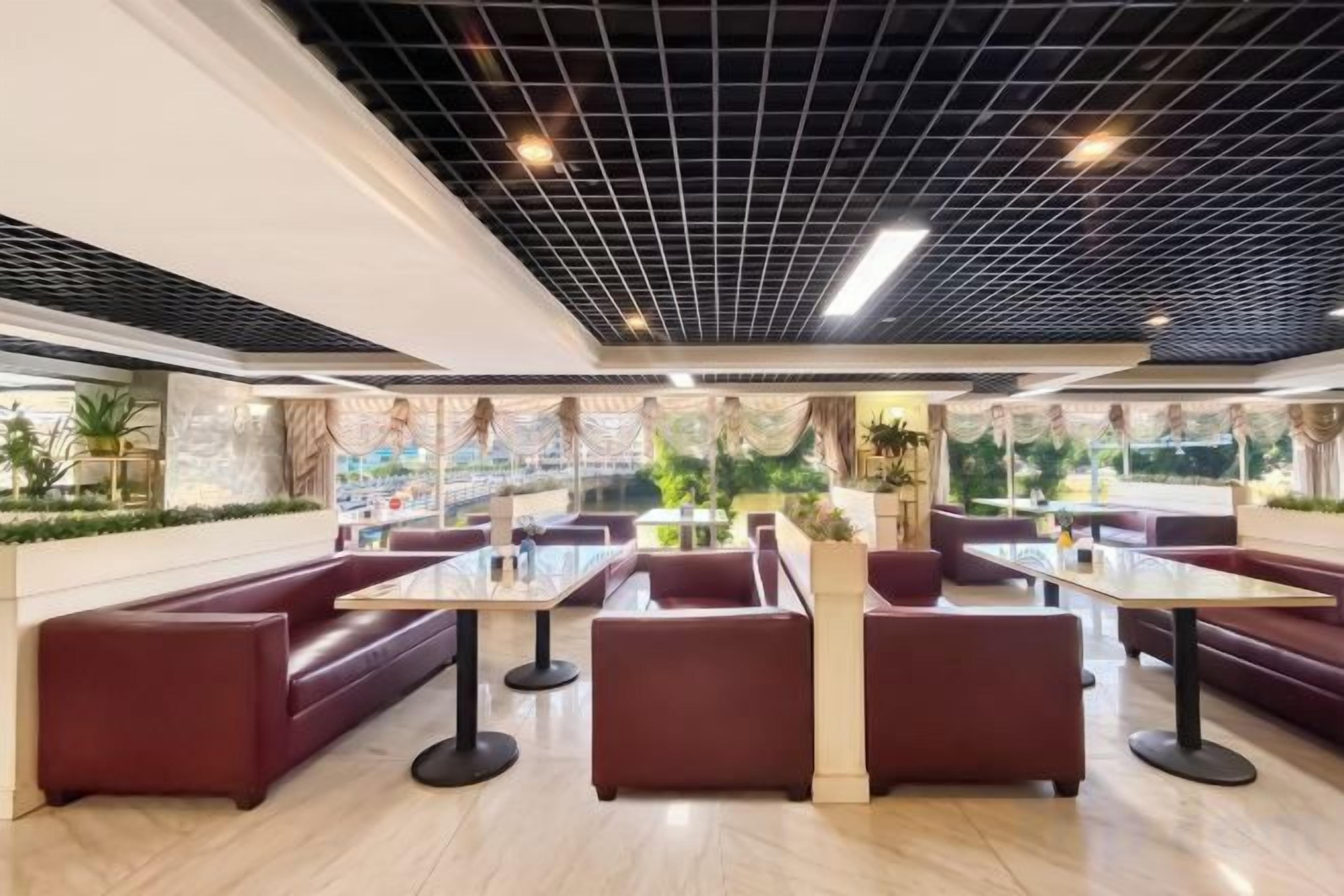 A modern restaurant with red seating, a grid ceiling, and a view of greenery outside.
