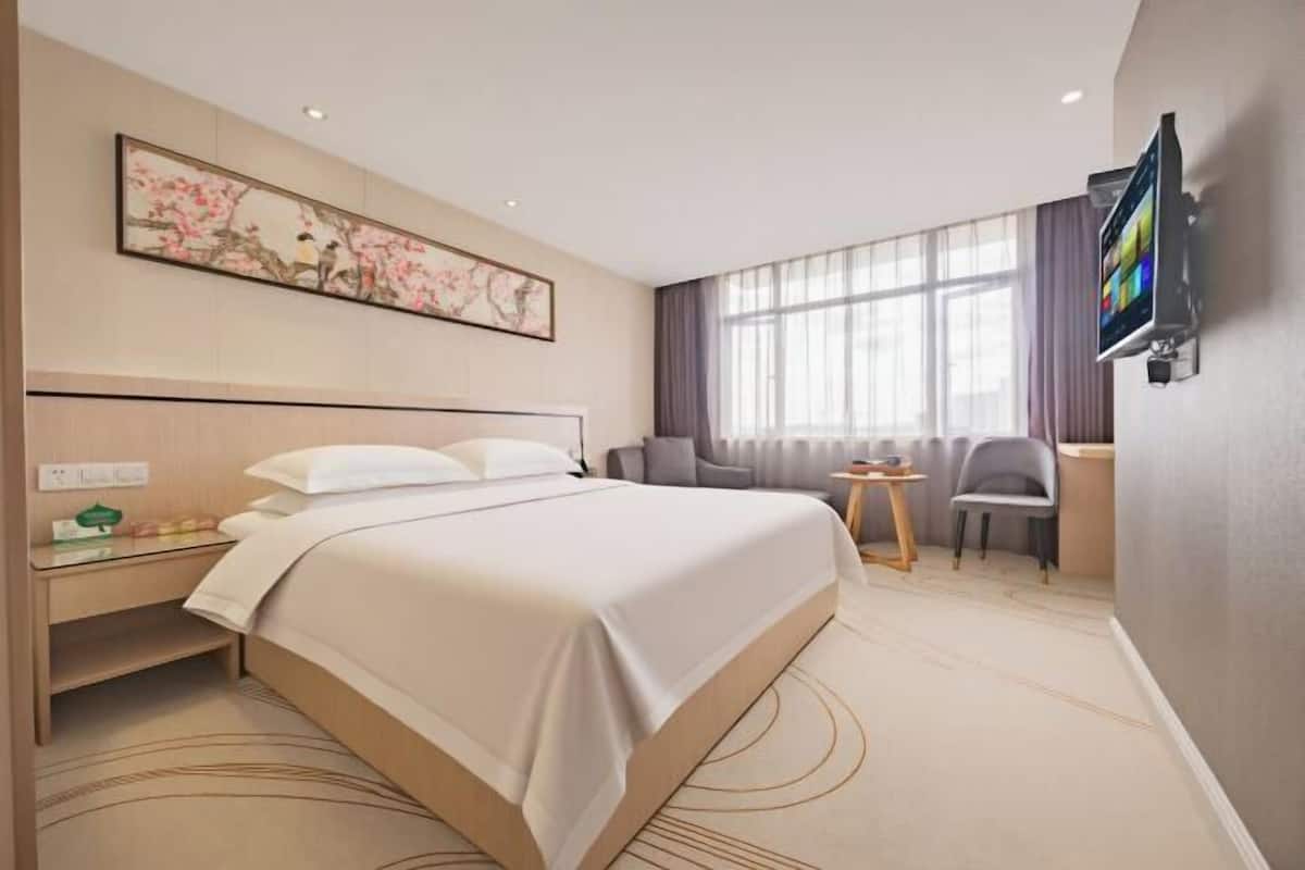 Camera d'albergo con un letto grande, una scrivania, una sedia, una televisione e una finestra con tende.