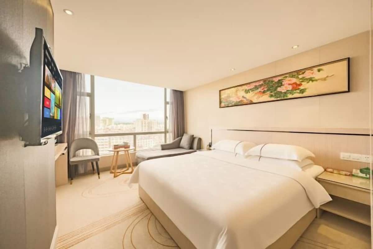 Una camera d'albergo con un letto grande, una scrivania con sedia, una televisione e una finestra vista città.