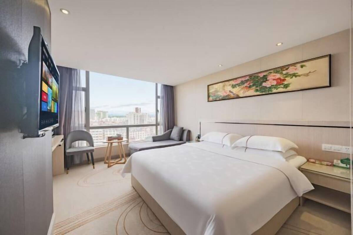Una camera d'albergo con un letto grande, una scrivania con un televisore, una sedia, un tavolino e un quadro appeso al muro.