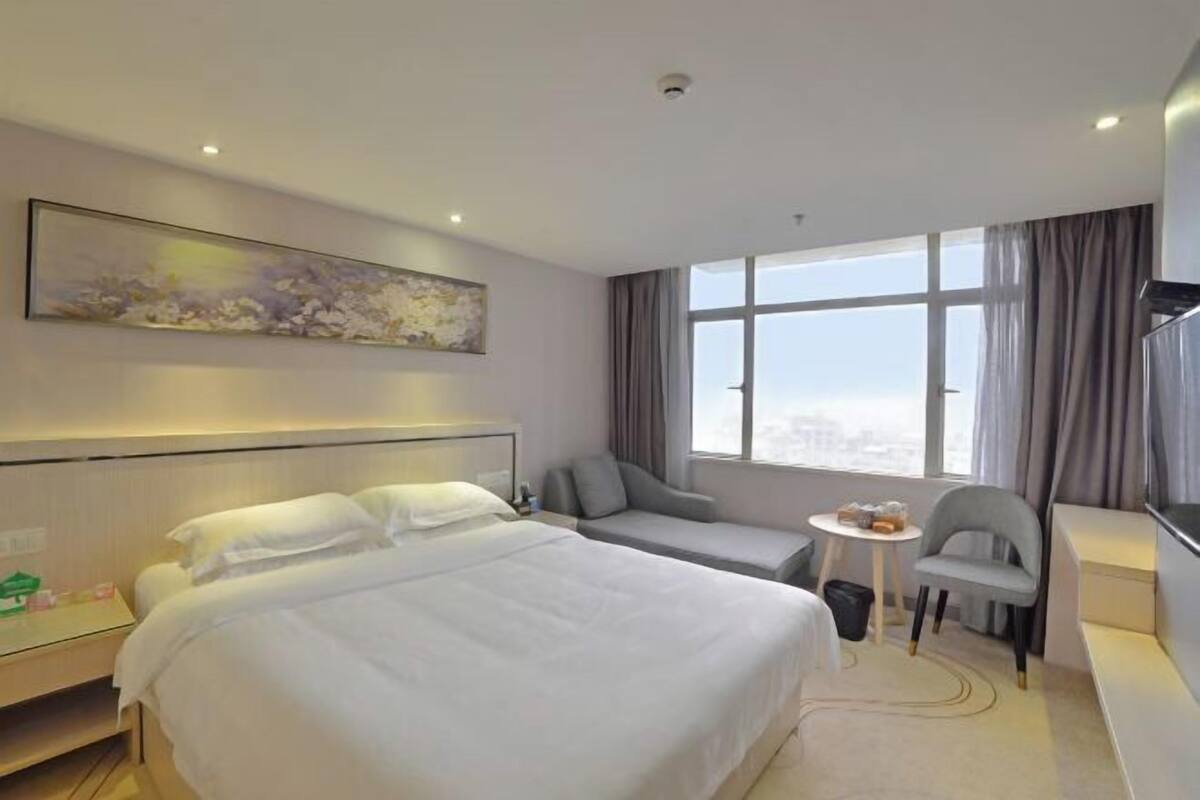 Camera d'albergo con un letto, una zona salotto, un piccolo tavolo, una sedia, una televisione e un'ampia finestra.