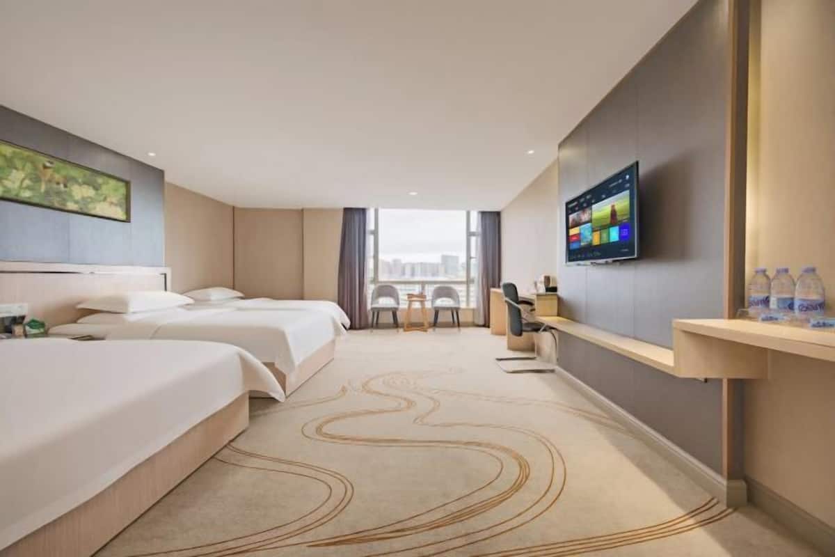 Camera d'albergo con due letti, una scrivania, una sedia, una televisione e vista sulla città.