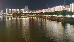 Un paisaje urbano nocturno con un río que refleja las luces de edificios y árboles.