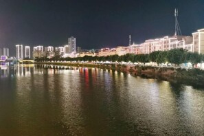 Ein nächtliches Stadtbild mit einem Fluss, der Lichter von Gebäuden und Bäumen reflektiert.