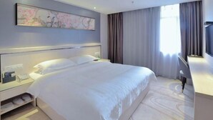 Moderni hotellihuone, jossa on suuri sänky, työpöytä ja televisio.