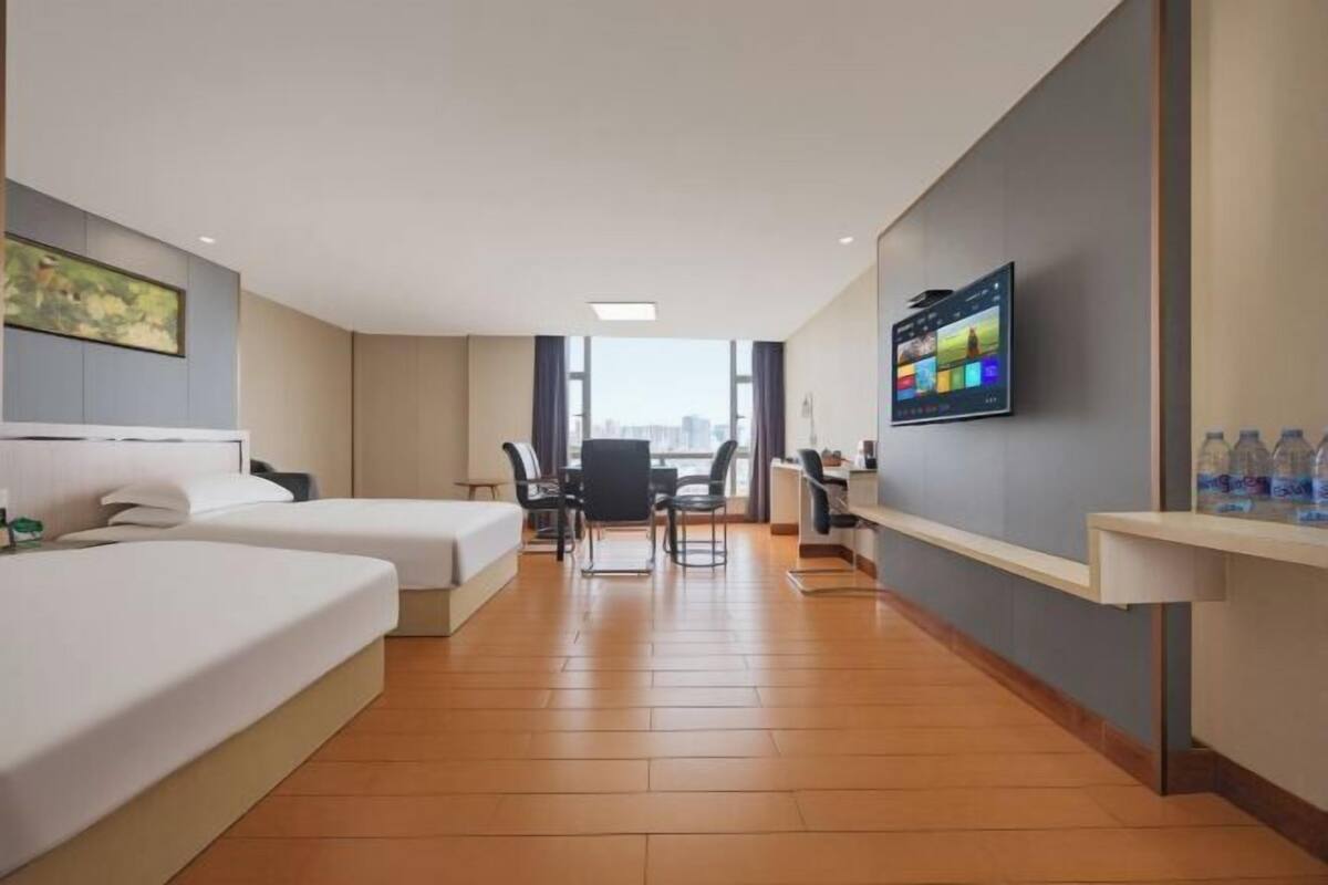 Camera d'hotel con due letti, una scrivania, una sedia, una televisione e una finestra con vista sulla città.