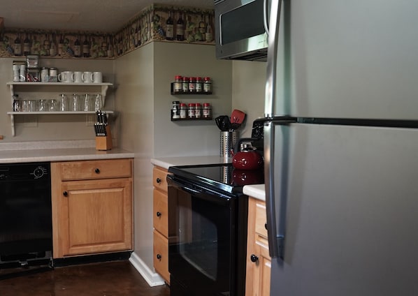 A kitchen with wooden cabinets, a stainless steel refrigerator, a microwave, and a red kettle.
