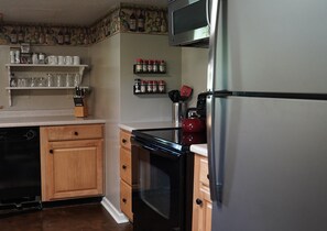 A kitchen with wooden cabinets, a stainless steel refrigerator, a microwave, and a red kettle.