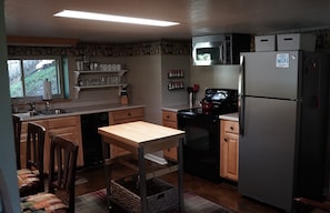 A compact kitchen with wooden cabinets, a stainless steel refrigerator, a microwave, and a stove. There is a window providing natural light and a small sink area.