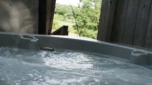 A hot tub with a view of a wooden deck and greenery.