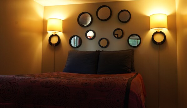 A hotel room with a bed, a headboard, and wall-mounted circular mirrors.