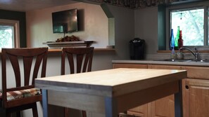 A kitchen with wooden cabinets, a dining table, chairs, a coffee maker, and a window with colorful bottles.