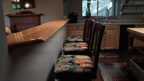 A kitchen with a wooden bench, a patterned chair, and a window with bottles on the counter.