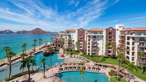 Ein Resort mit mehreren Gebäuden, einem zentralen Poolbereich und Blick auf den Ozean.