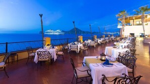 Ein Restaurant mit Außenbereich und Meerblick, ausgestattet mit Tischen und Stühlen mit weißen Tischdecken.