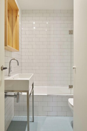 A bathroom with white tiled walls, a white sink, a bathtub, and a wooden cabinet. - Pagoa Suite by FeelFree Rentals (San Sebastian)