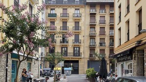 Um edifício com vários andares, varandas, fachada comercial e veículos estacionados.