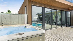 Ein moderner Außenbereich mit Whirlpool, einer Holzterrasse und Glastüren zu einer Terrasse.