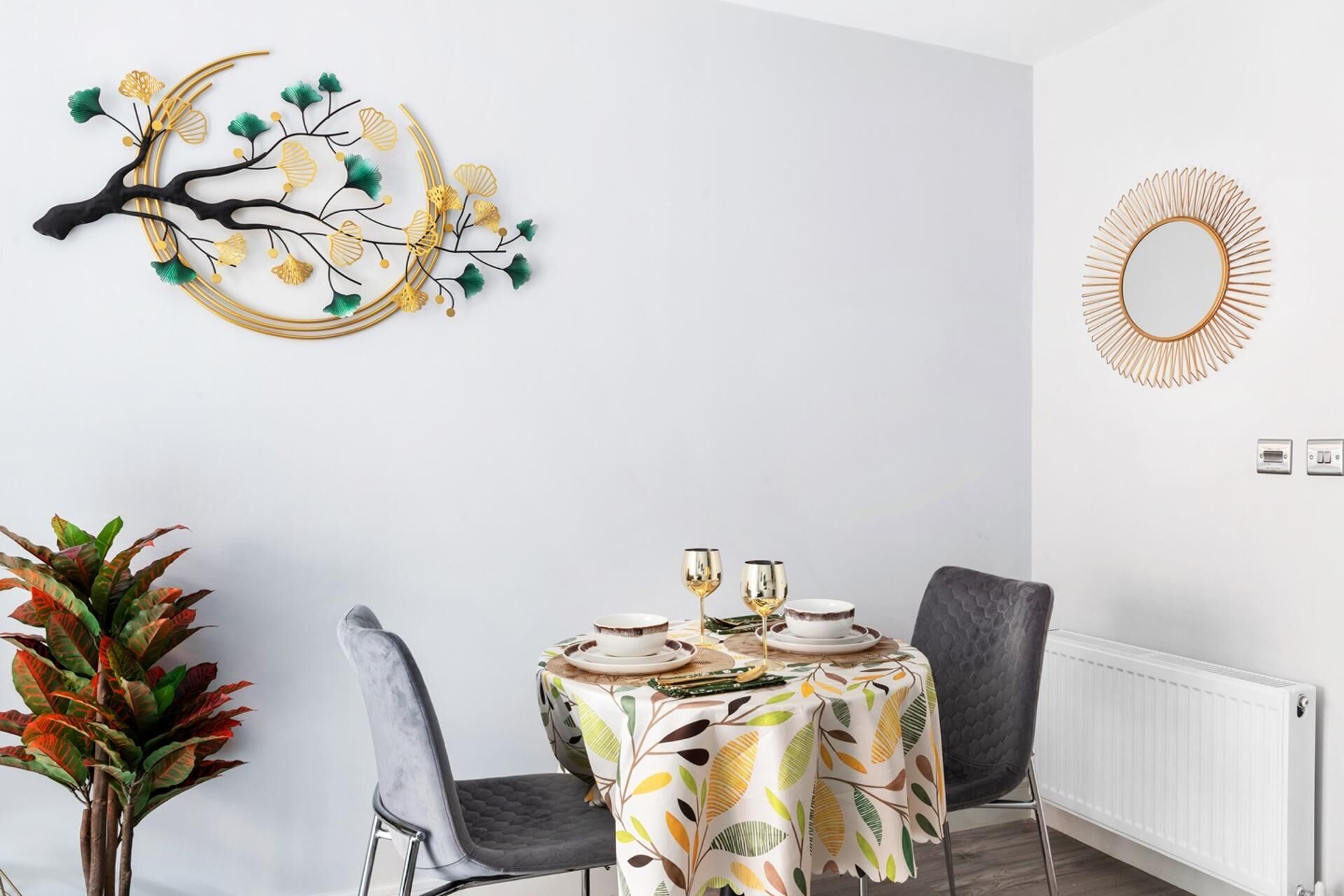 Een eetgedeelte met een tafel gedekt voor twee personen, een decoratief kunstwerk en een radiator.