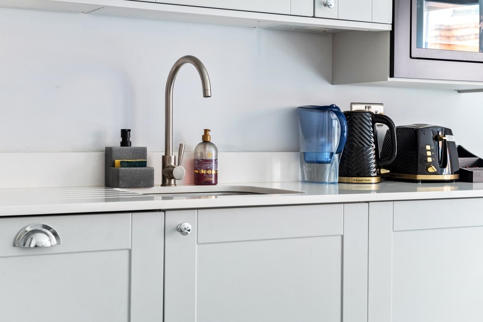 Una cocina moderna con un grifo de acero inoxidable, una cafetera, un dispensador de agua y un dispensador de jabón en la encimera.
