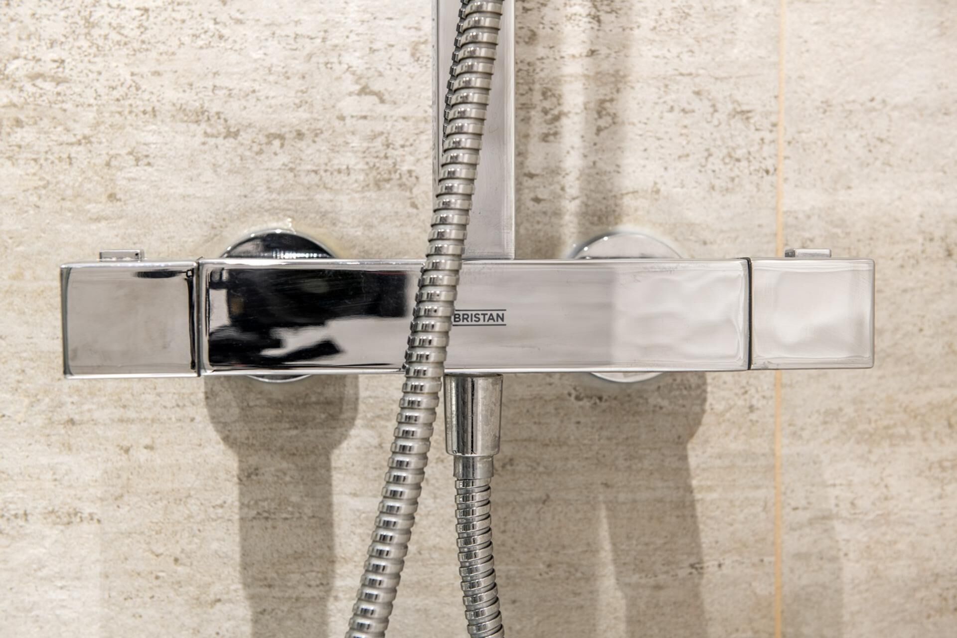 A chrome shower control with a flexible hose, mounted on a textured wall.