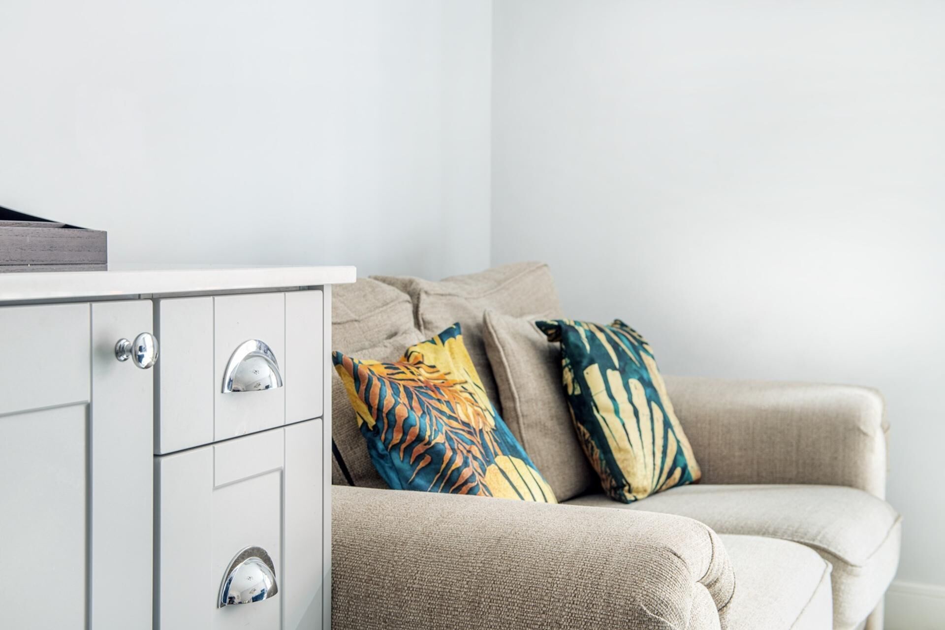 A minimalist living room with a white cabinet, a beige sofa, and patterned throw pillows.