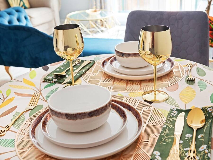 A dining table set with white plates, gold cutlery, and two gold wine glasses.