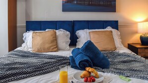 A hotel room with a bed, a painting of a pier and a Ferris wheel, a nightstand with a lamp, and a breakfast tray with croissants and strawberries. - A spacious property perfect for families and friends. (Bispham, near Blackpool)