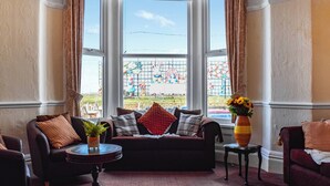 A room with a bay window, a sofa, a small table, and a vase with flowers. - A spacious property perfect for families and friends. (Bispham, near Blackpool)