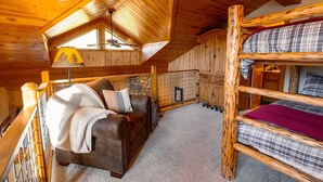 A cozy cabin interior with a wooden ceiling, a bunk bed, a sofa, and a window with a view of trees.