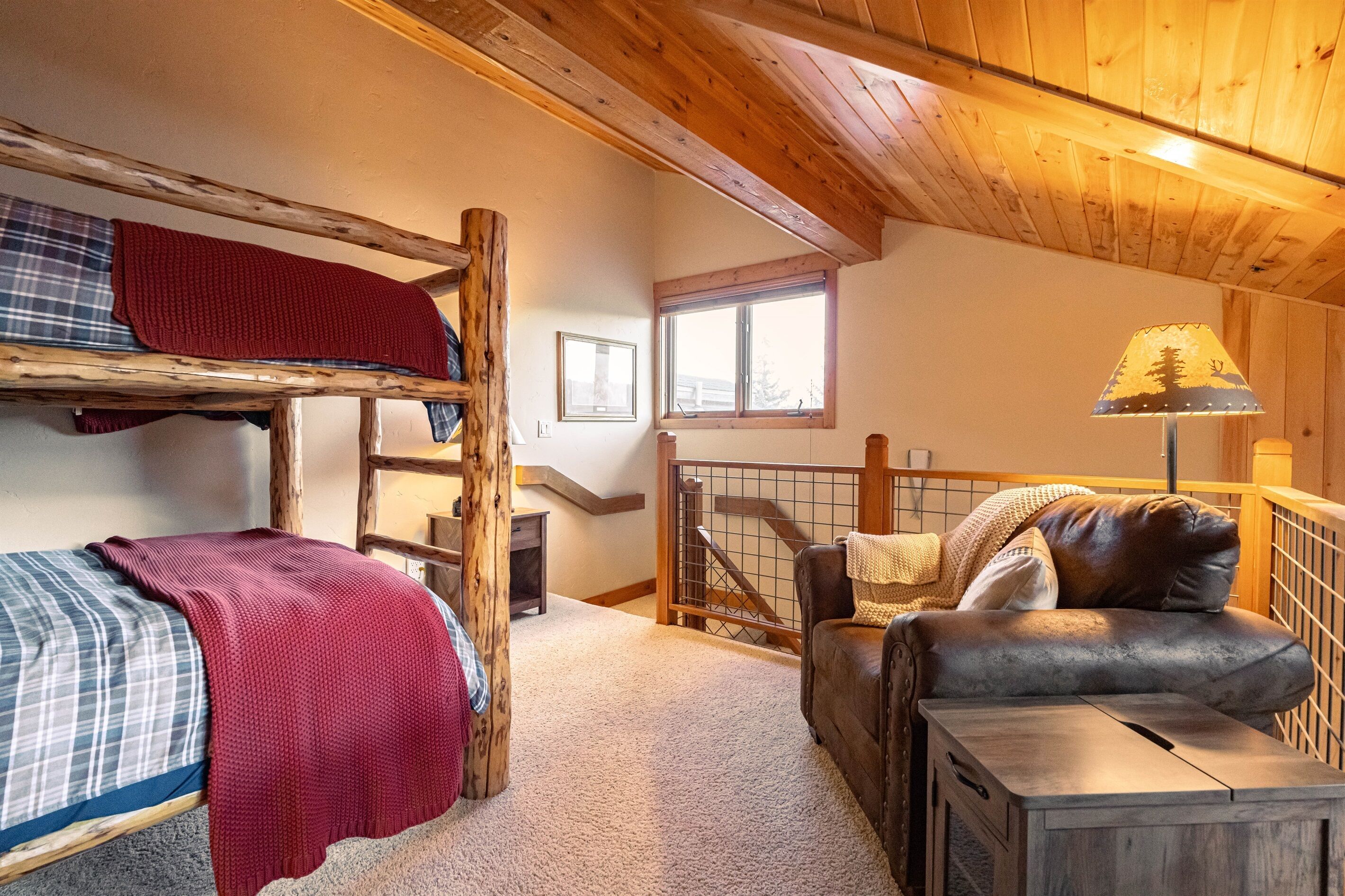 A cozy room with a bunk bed, a couch, a lamp, and a window.