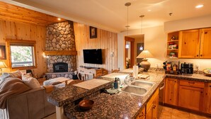 A cozy kitchen with wooden walls, a stone fireplace, granite countertops, and wooden cabinets.