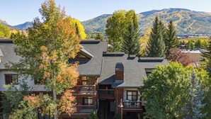 A multi-story lodge with a stone facade, a balcony with outdoor seating, and a view of mountains in the background.