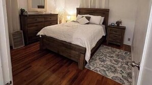 Ein Schlafzimmer mit einem hölzernen Bett, einem Schminktisch, einem Spiegel und einem gemusterten Teppich.